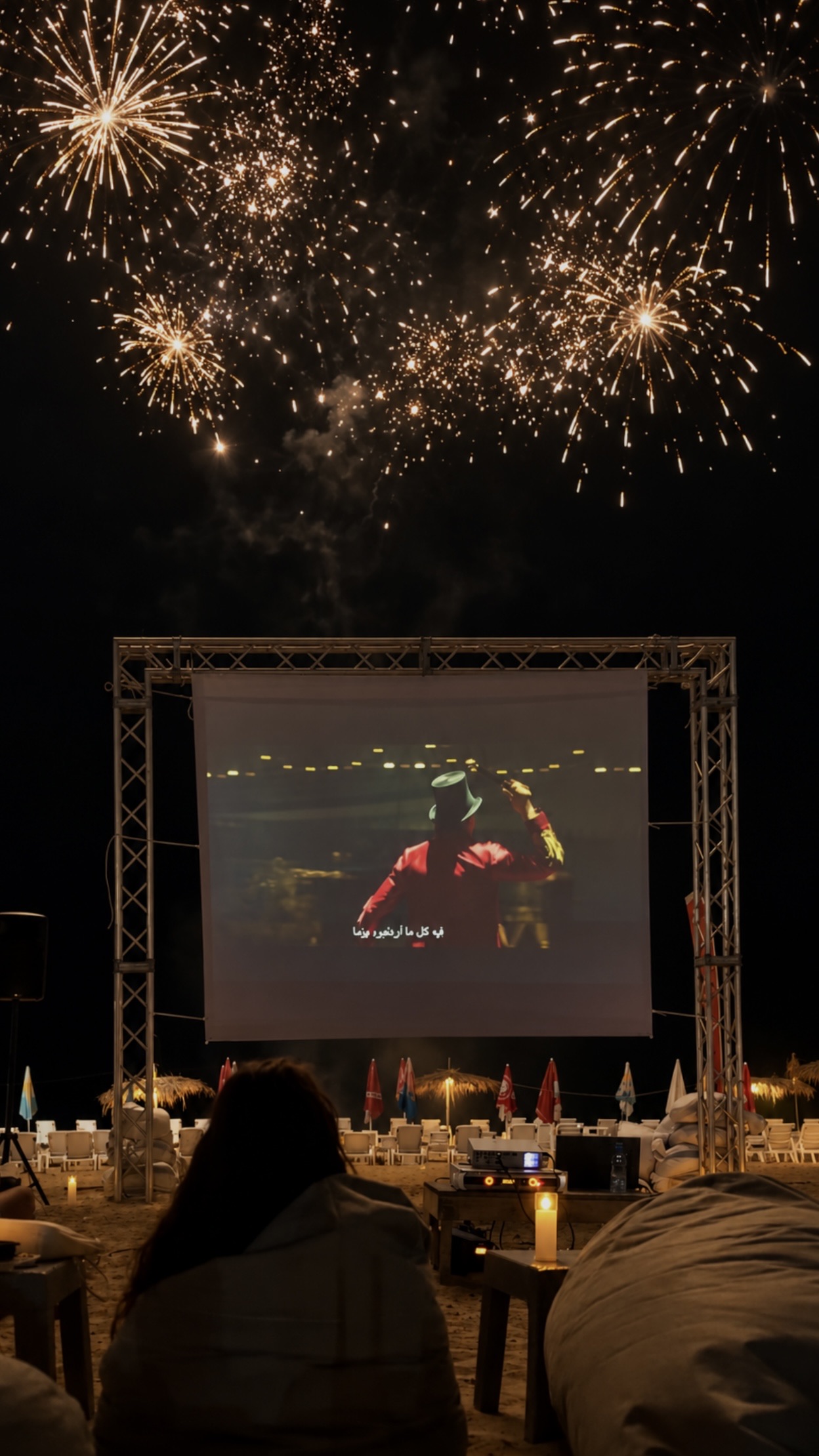 Fireworks over the lit screen on the sand at C Lemon, Okaibe, beanbags and candles across the beach and the sea beyond